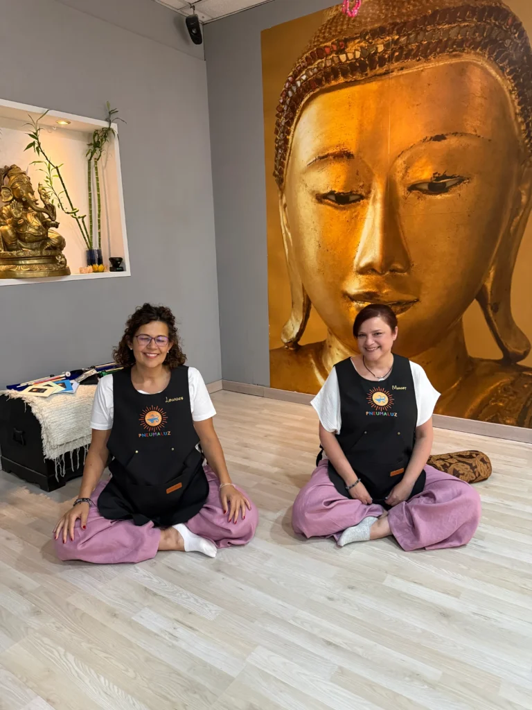 Lourdes y Margot, del equipo de PneumaLuz, sentadas en postura de meditación frente a un mural de Buda